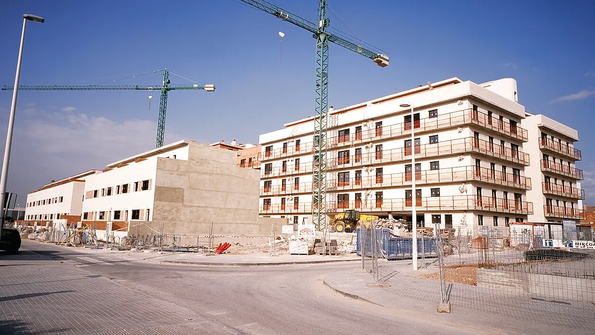 Promoción residencial en construcción con dos grúas torre, la visita de obra que llega tras revisar documentos y organismos